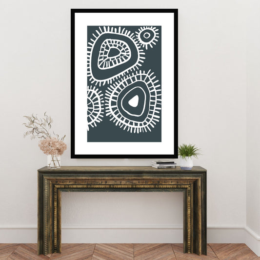 Plakat i abstrakt grafisk motiv i hvit dekor og mørk blå/grå bunnfarge. Plakaten har en hvit kant som gir dybde, og fremhever motivet. Illustrasjonen viser plakat i sort ramme som henger på en vegg over en liten skjenk.