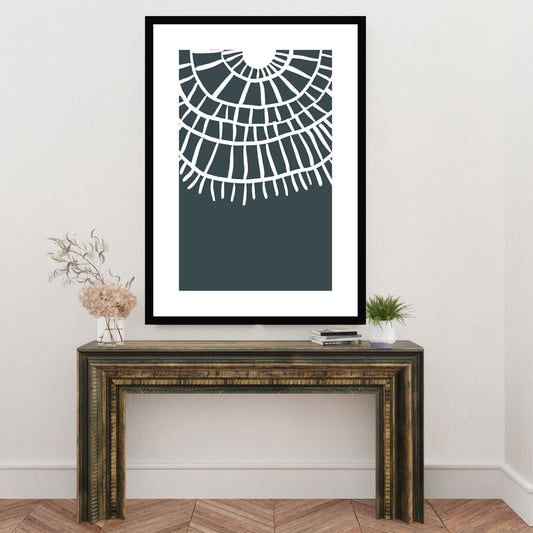 Plakat i abstrakt grafisk motiv i hvit dekor og mørk blå/grå bunnfarge. Plakaten har en hvit kant som gir dybde, og fremhever motivet. Illustrasjonen viser plakat i sort ramme som henger på en vegg over en liten skjenk.