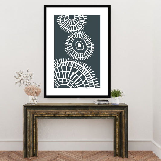 Plakat i abstrakt grafisk motiv i hvit dekor og mørk blå/grå bunnfarge. Plakaten har en hvit kant som gir dybde, og fremhever motivet. Illustrasjonen viser plakat i sort ramme som henger på en vegg over en liten skjenk.