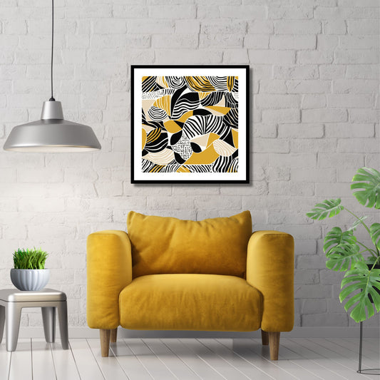 Kvadratisk plakat med abstrakt mønster i fargene oker, sort og hvit. Det er en hvit kant rundt plakaten. Her er den rammet inn i sort ramme, og henger på en hvit murvegg. Det henger en grå pendellampe og det står en gul stol under bildet.