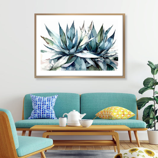 Grafisk akvarell av en praktfull Aloe Vera plante i grågrønne fargenyanser, mot en ren hvit bakgrunn. Illustrasjonsfoto viser motivet som plakat i en lys ramme som henger over en sofa.