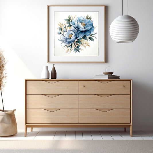 Grafisk motiv av blå blomster med grønt bladverk. Motivet fås som plakat og på lerrett. Miljøbilde av motiv i eikeramme på en vegg over en komode.