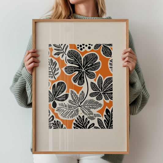 Bold Botanica kombinerer kraftige, svarte bladformer med en varm oransje bakgrunn i retroinspirert design. Illustrasjon viser motiv med bred kant i eik ramme.