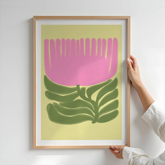 Bold botanic No1 er et stilisert botanisk motiv med en stor, lys rosa blomst som strekker seg utover som en solfane. Bladverket under er malt i dype grønntoner og gir et mykt, bølgende uttrykk mot den lysegule bakgrunnen. Illustrasjon viser motivet i eik ramme.