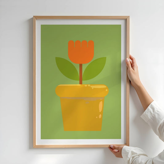 Bold Botanical No10 er en enkel og ikonisk blomst i kraftig oransje står rank i en gyllen blomsterpotte. Med to mørkegrønne blader og en stilisert form mot en frisk grønn bakgrunn, formidler motivet både retroglede og moderne minimalisme. Illustrasjon viser plakat i eik ramme.