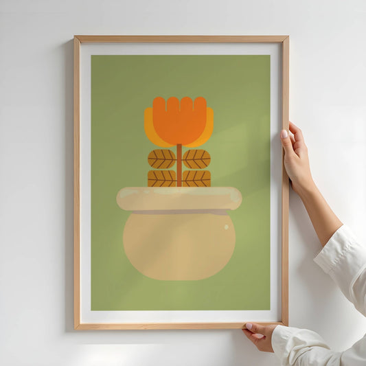 Bold Botanical No15 viser en stilisert blomst i varme oransje og gule toner står oppreist i en rund, gyllen potte med blank glasur. Fire symmetrisk plasserte blader i brunt med mørke årer tilfører en geometrisk ro, mens den olivengrønne bakgrunnen skaper et harmonisk bakteppe. Illustrasjon viser plakat med eik ramme.