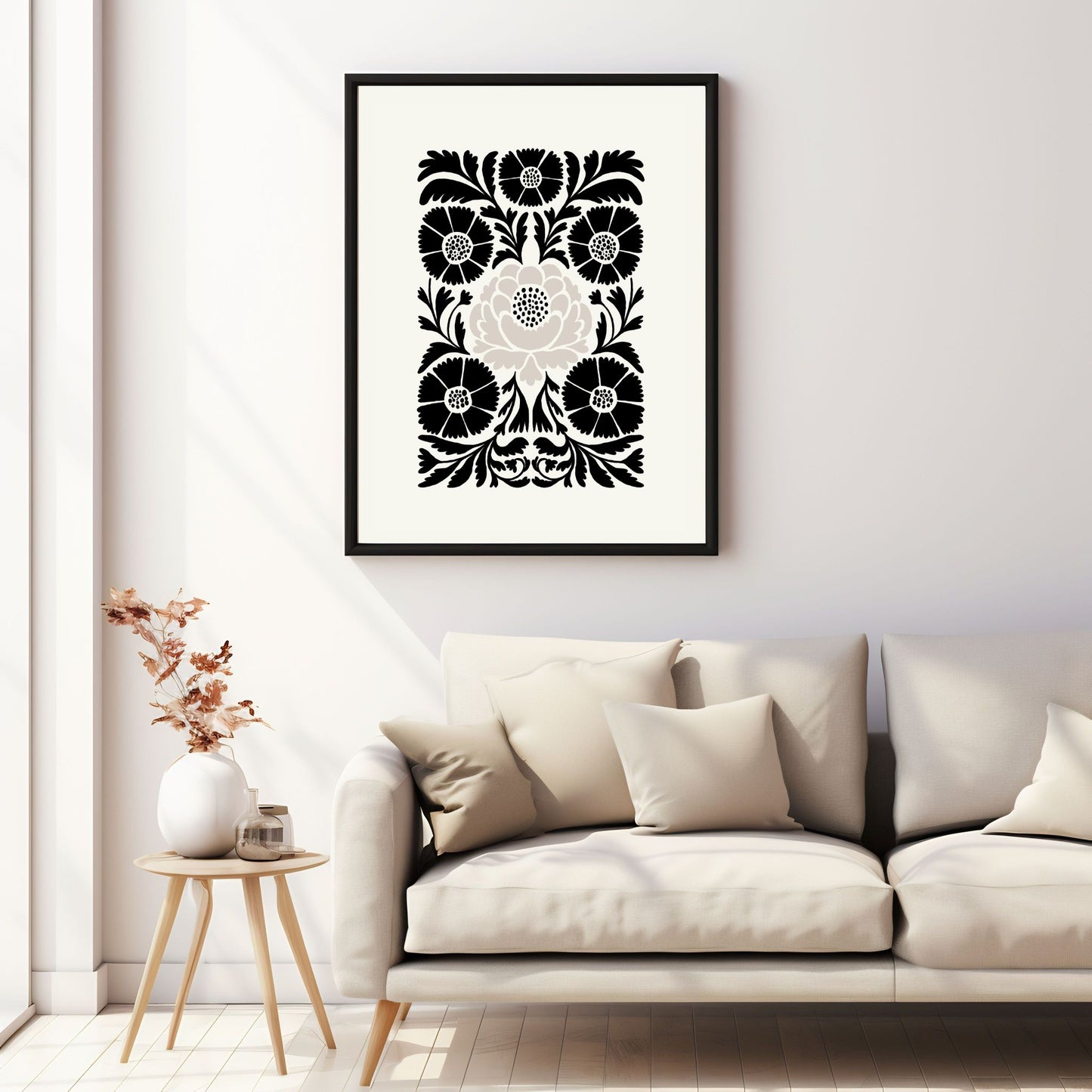 Illustrasjon av en grafisk plakat i abstrakt, floralt mønster i sort, beige og dempet hvit bakgrunn. Plakaten har en bred kant i samme som bakgrunnsfarge, og henger i sort ramme på en vegg over en sofa.