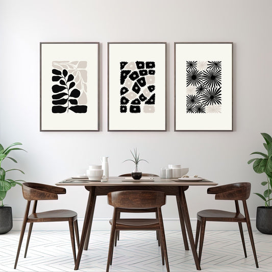 Miljøbilde som viser denne grafiske plakaten i abstrakt, floralt mønster i sort, beige og dempet hvit bakgrunn. Plakaten har et bredt felt rundt i bakgrunnsfarge, og henger i sort ramme på en lys vegg over et spisebord. Ved siden henger to bilder fra samme serie.