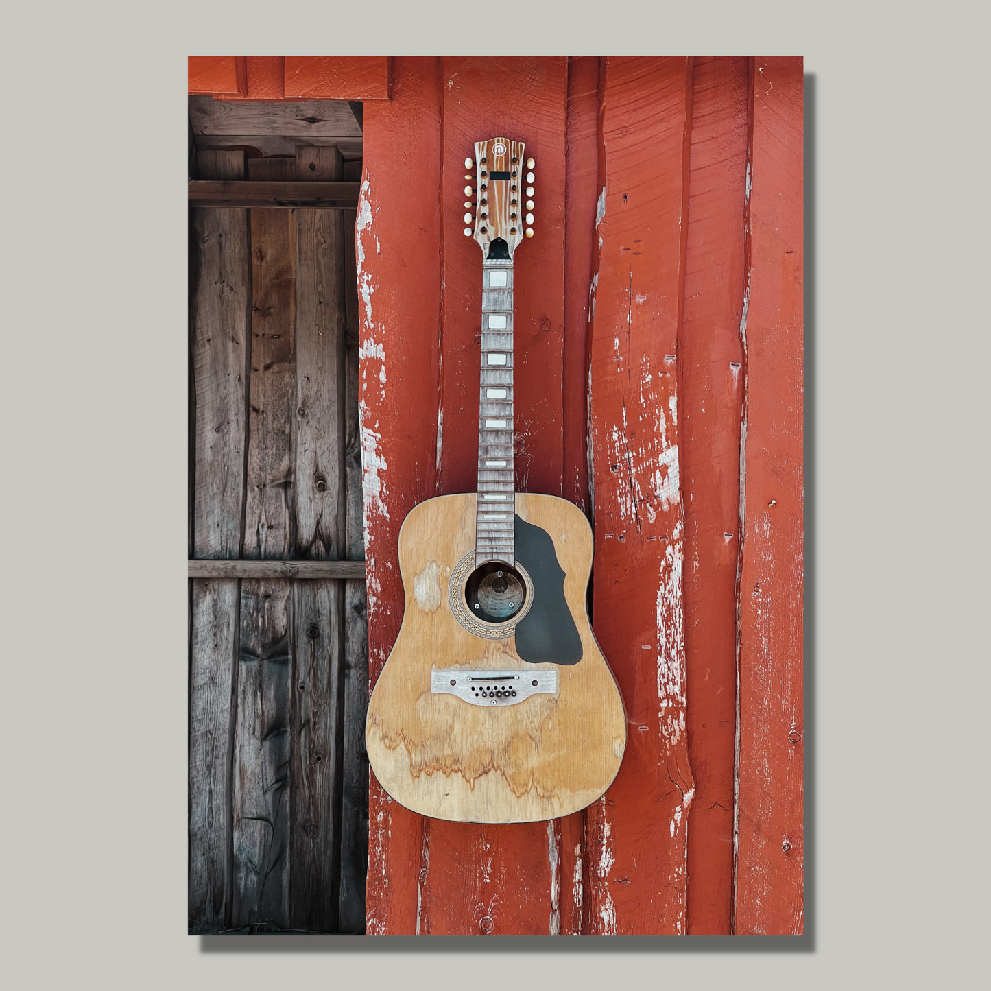 Motivet av en slitt og velbrukt kassegitar som henger på det rødmalte buss-stoppet på Toftarøyna fanger essensen av norsk kystkultur på en vakker og nostalgisk måte. Illustrasjonsfoto viser motivet på lerret.