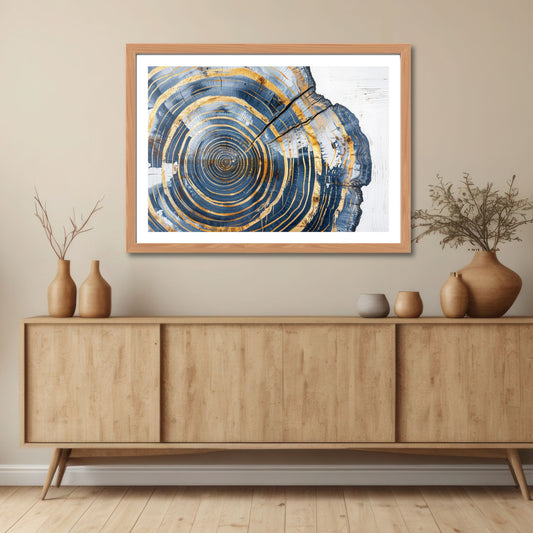 Dette unike kunstverket fanger essensen av naturens mønstre, med konsentriske sirkler inspirert av treets årringer, kombinert med stilige gull- og blåtoner. Illustrasjon viser motivet som plakat med hvit kant i lys ramme.