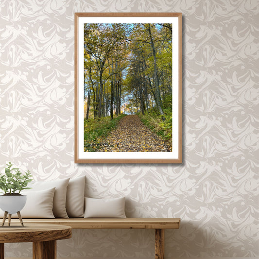 Bildet viser en fredelig skogsvei dekket av gyllent løv og omkranset av høstfargede trær – en visuell påminnelse om naturens rolige puls. Illustrasjon viser motivet som plakat med hvir kantlinje i eik ramme.