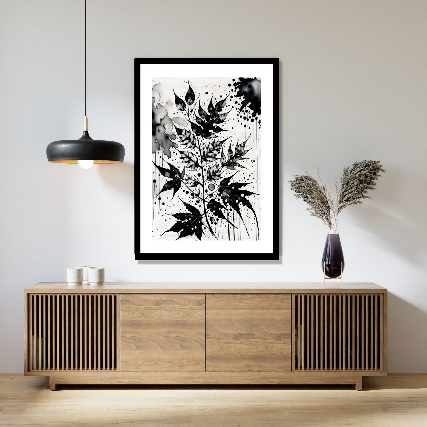 Miljøbildet viser en grafisk plakat i abstrakt, floralt mønster i sort-hvitt. Plakaten som har en dekorativ hvit kant, henger i en sort ramme over en skjenk i teak. Ved siden henger en sort lampe og på skjenken står det en sort vase med strå.