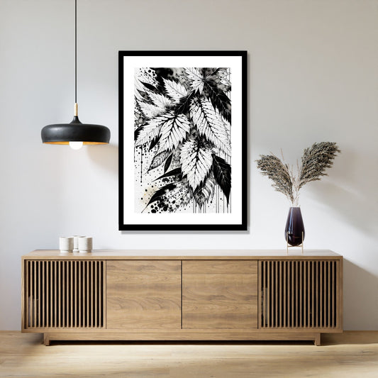 Miljøbildet viser en grafisk plakat i abstrakt, floralt mønster i sort-hvitt. Plakaten som har en dekorativ hvit kant, henger i en sort ramme over en skjenk i teak. Ved siden henger en sort lampe og på skjenken står det en sort vase med strå.