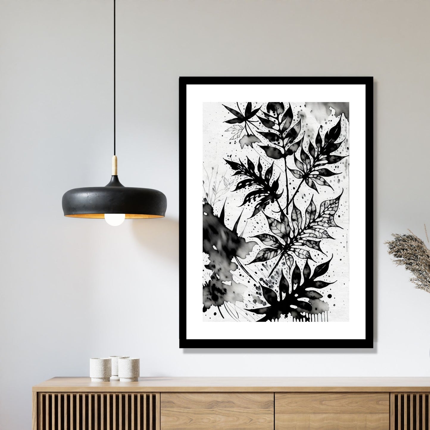 Miljøbildet viser en grafisk plakat i abstrakt, floralt mønster i sort-hvitt. Plakaten som har en dekorativ hvit kant, henger i en sort ramme over en skjenk i teak. Ved siden henger en sort lampe.