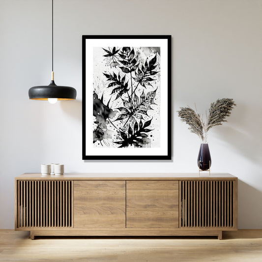 Miljøbildet viser en grafisk plakat i abstrakt, floralt mønster i sort-hvitt. Plakaten som har en dekorativ hvit kant, henger i en sort ramme over en skjenk i teak. Ved siden henger en sort lampe og på skjenken står det en sort vase med strå.