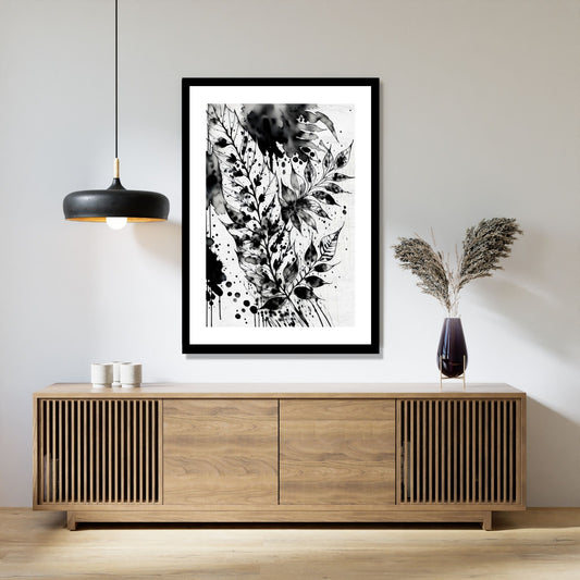 Miljøbildet viser en grafisk plakat i abstrakt, floralt mønster i sort-hvitt. Plakaten som har en dekorativ hvit kant, henger i en sort ramme over en skjenk i teak. Ved siden henger en sort lampe og på skjenken står det en sort vase med strå.