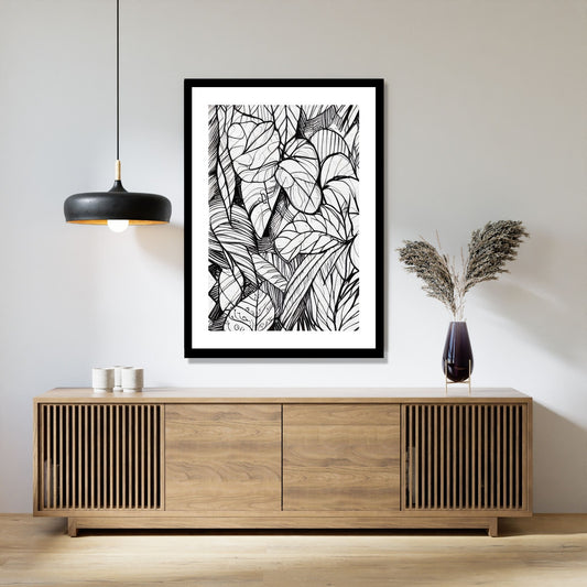 Miljøbildet viser en grafisk plakat i abstrakt, floralt mønster i sort-hvitt. Plakaten som har en dekorativ hvit kant, henger i en sort ramme over en skjenk i teak. Ved siden henger en sort lampe og på skjenken står det en sort vase med strå.