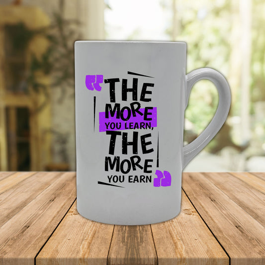 Krus i hvit keramikk med håndtak. Kruset er påført teksten "The more you learn, the more you earn" Sort farge på tekst og lilla dekorelement.