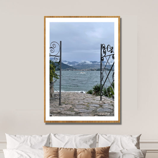 En regntung og vindfull augustdag i Stresa ved Lago Magiore, Piemonte. En grind i smijern står åpen og det er adkomst til sjøen. En båt duver i bølgene. Alpene med lavt skydekke, og byen Verbania kan ses i det fjerne.