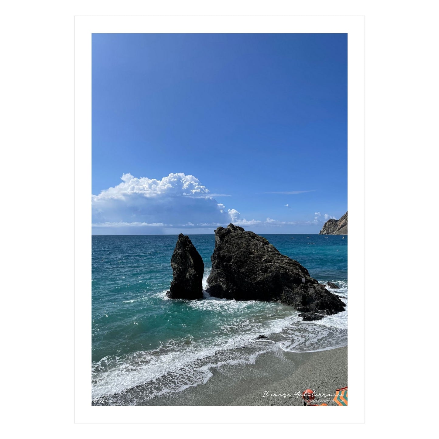 Motiv fra stranden ved Montereosso al Mare, en av de fem byene i Cinque Terre ved Liguriakysten i Italia. Bildet viser blått middelhav og himmel som møter havet i horisonten. . I overgangen mellom himmel og hav ligger en stor skybanke. Det slår små bølger inn mot den karakteristiske klippen som ligger midt på stranden