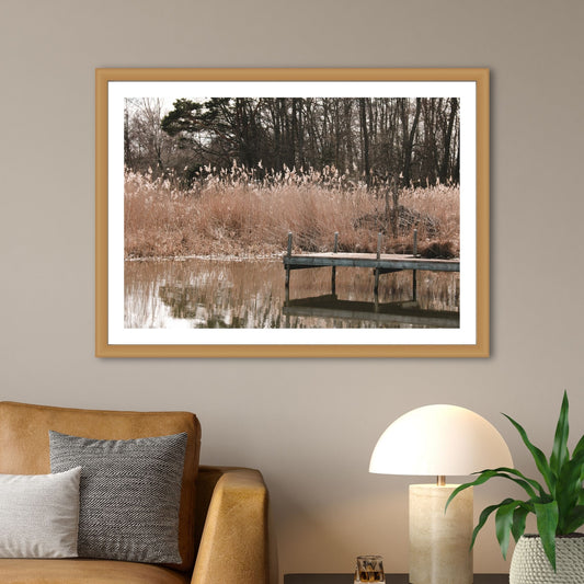 Denne vakre fotoplakaten fanger øyeblikket da solen kaster sine gyldne stråler over Mälaren, og avslører en pittoresk brygge som speiler seg i det rolige vannet. Illustrasjon som viser motivet som plakat i en ramme av eik.