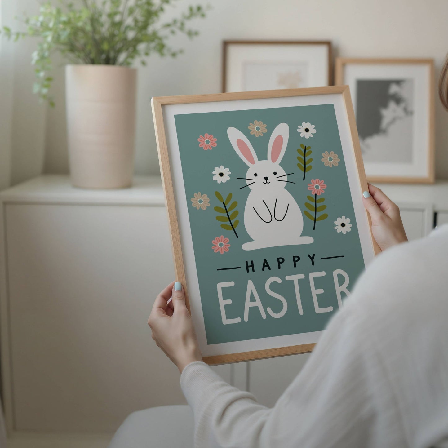 Denne stilrene påskeplakaten har et elegant design med en søt hvit påskehare omgitt av delikate vårblomster og naturlige blader, perfekt satt mot en beroligende grønn bakgrunn. Illustrasjon viser plakat med hvit kant i eik ramme.