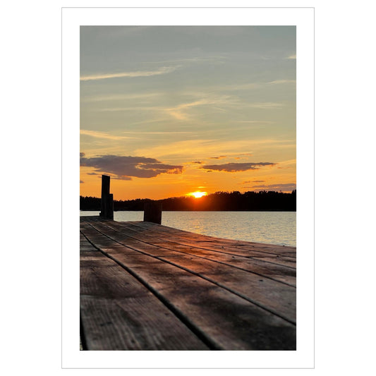Nydelig solnedgang ved Krokstadfjorden ved Saltnes. Motiv av en brygge som går ute i sjøen, og en sol som er i ferd med å gå ned på en oransje himmel. Fås både som plakat og på lerret.