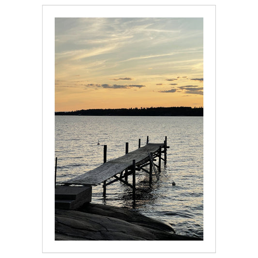 Nydelig solnedgang ved Krokstadfjorden ved Saltnes. Motiv av en brygge som går ute i sjøen, og en sol som er i ferd med å gå ned på en oransje himmel. Fås både som plakat og på lerret.
