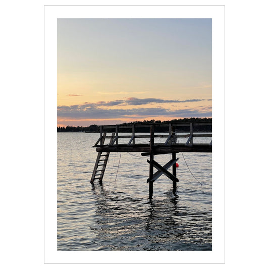 Nydelig solnedgang ved Krokstadfjorden ved Saltnes. Motiv av en brygge som går ute i sjøen, og en sol som er i ferd med å gå ned på en oransje himmel. Fås både som plakat og på lerret.