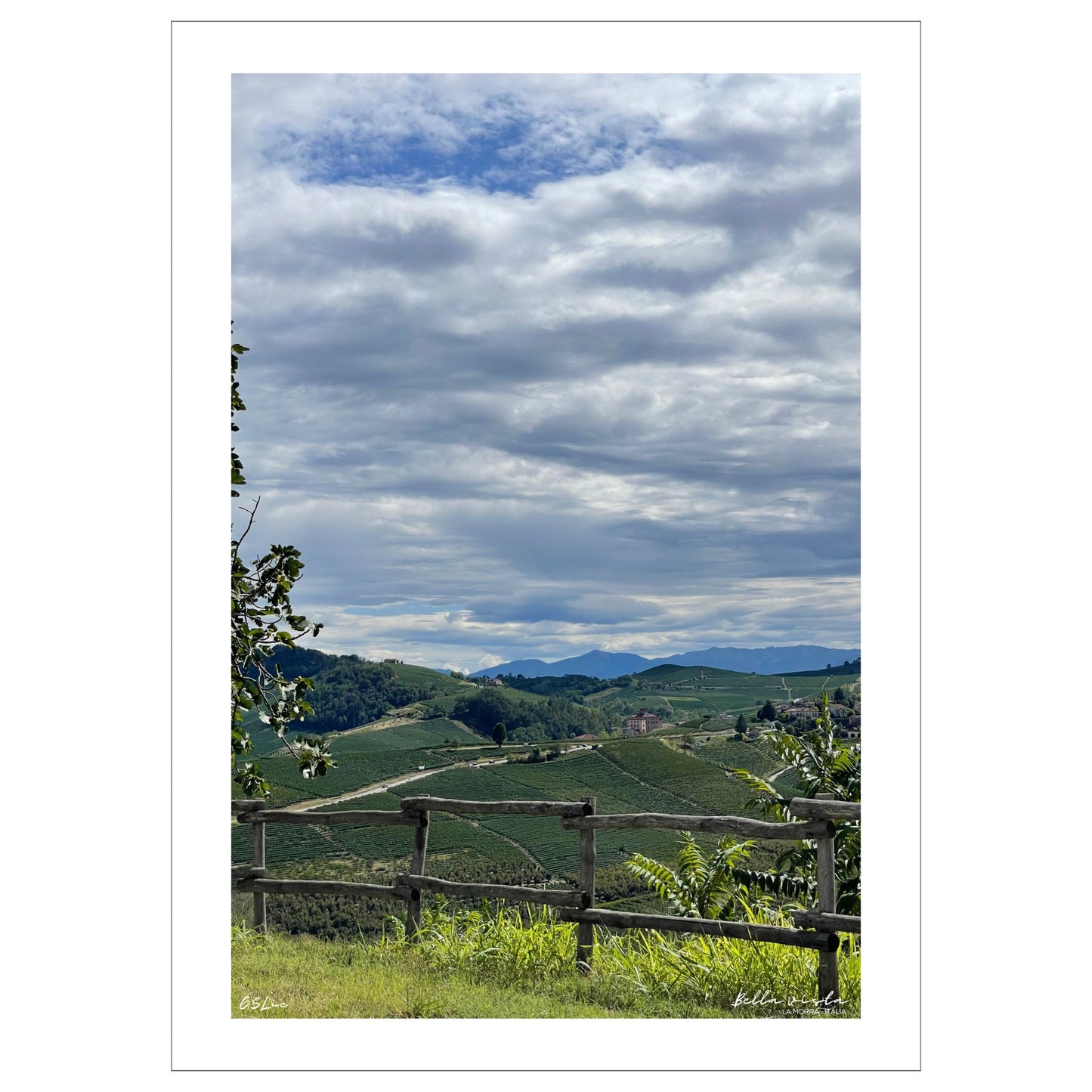 Utsikt mot Barolo fra vinmarker i La Morra området. Alpene kan skimtes i det fjerne. I forkant er det et tre gjerde. Det er et tett skylag på himmelen med en liten åpning hvor det skimtes blå himmel.