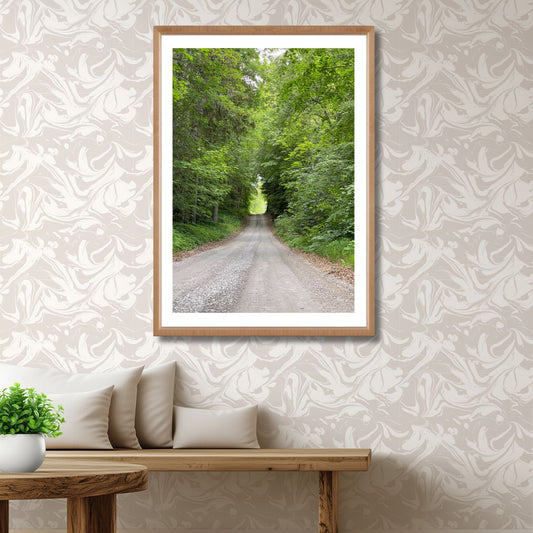 Med tett løvverk på begge sider og et naturlig lys som venter i enden av veien, inviterer motivet til ro, ettertanke og turlyst. Illustrasjon viser motivet som plakat med hvit kantlinje i eik ramme.