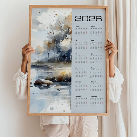 Kalender 2026 med akvarellmotiv av høstlig landskap ved vann, i lyse og varme toner. Illustrasjon viser kalender i eik ramme.
