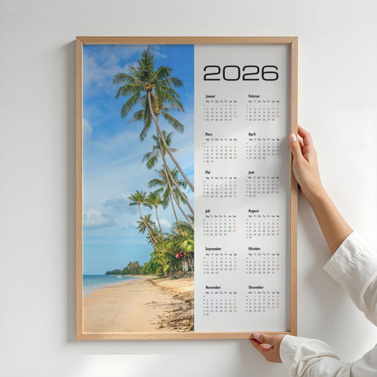 Kalender 2026 med motiv av eksotisk strand og høye palmer mot blå himmel, med tydelig kalenderdel og norske merkedager. Illustrasjon viser kalender i eik ramme.