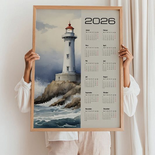 Kalender 2026 med akvarellmotiv av fyrtårn på klipper omgitt av bølger. Illustrasjon viser kalender i eik ramme.
