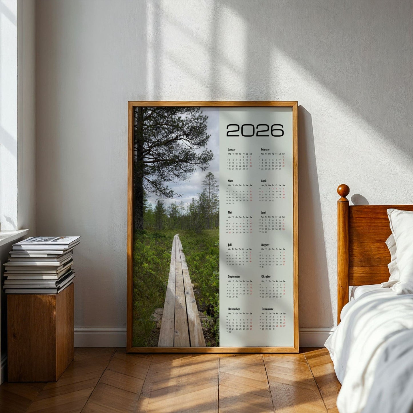 Kalender 2026 med foto av plankesti omgitt av grønne trær ved Øyingen. Illustrasjon viserkalender i eik ramme på et soverom.