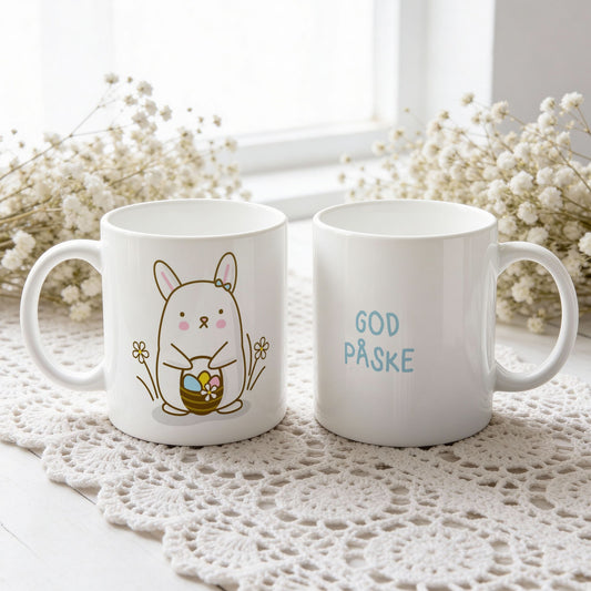 Hvitt keramikkrus med søt påskehare med sløyfe og kurv med påskeegg, samt teksten God påske i blå tone på motsatt side.