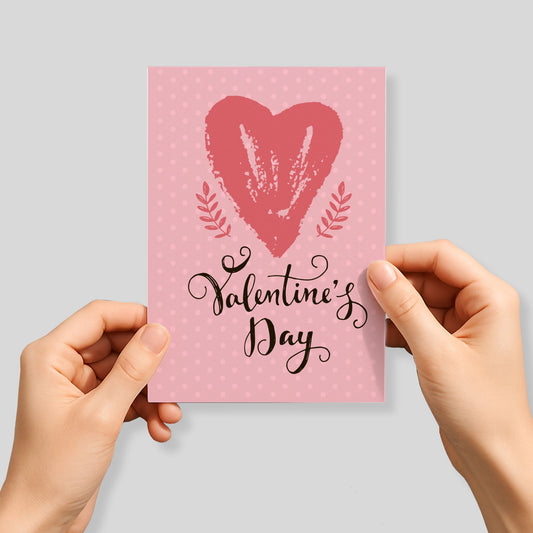 Kjærlighetskort med teksten Valentine’s Day, stort håndmalt hjerte og rosa prikket bakgrunn med botaniske detaljer. Person som holder kortet.