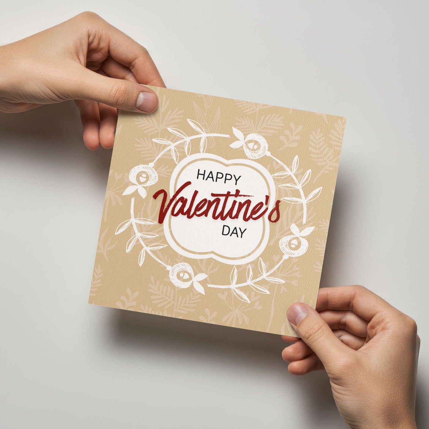 Valentineskort med teksten Happy Valentine’s Day, dekorativ blomsterkrans og botaniske detaljer i varme beige toner. Kortet blir holdt av en person.