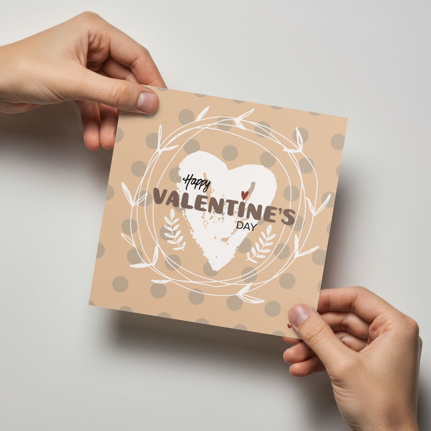 Valentineskort med teksten Happy Valentine’s Day, håndmalt hjerte og dekorativ krans i myke beige og naturtoner. Kortet blir holdt av en person.