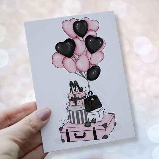 Valentineskort med rosa og sorte hjerteballonger, gaver, høye hæler og veske i et stilrent og feminint design. Kortet holdes i en hånd.
