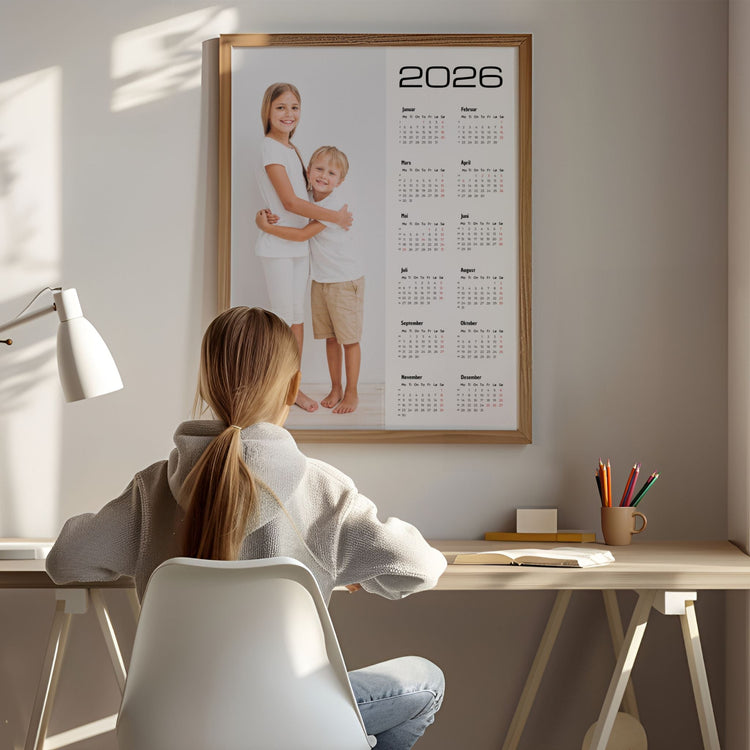 Personlig kalender 2026 i ramme med barnebilde, plassert over skrivebord i hjemmekontor.