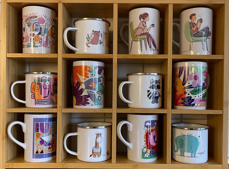 Hylle med keramikk- og emaljekrus i ulike farger og illustrerte motiver, inkludert dyr, mennesker og abstrakte design