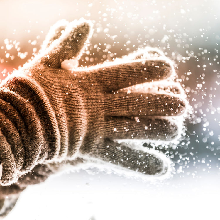 Nærbilde av ullvotter som klapper snø i vinterlys – en varm og stemningsfull introduksjon til vinterens plakater.