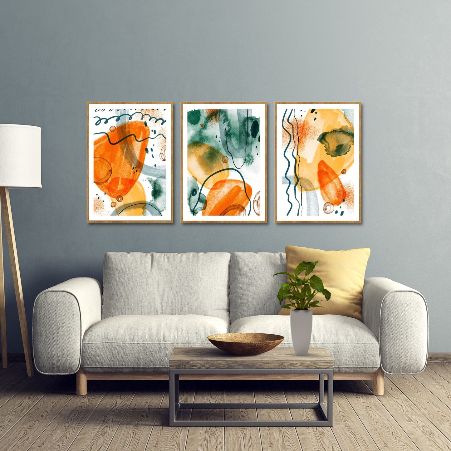 3 grafiske kunst plakater med abstrakt mønster. Fargenyanser i oransje og grønn på hvit bunn. Bildet viser plakater på en vegg, hengende over en beige sofa.