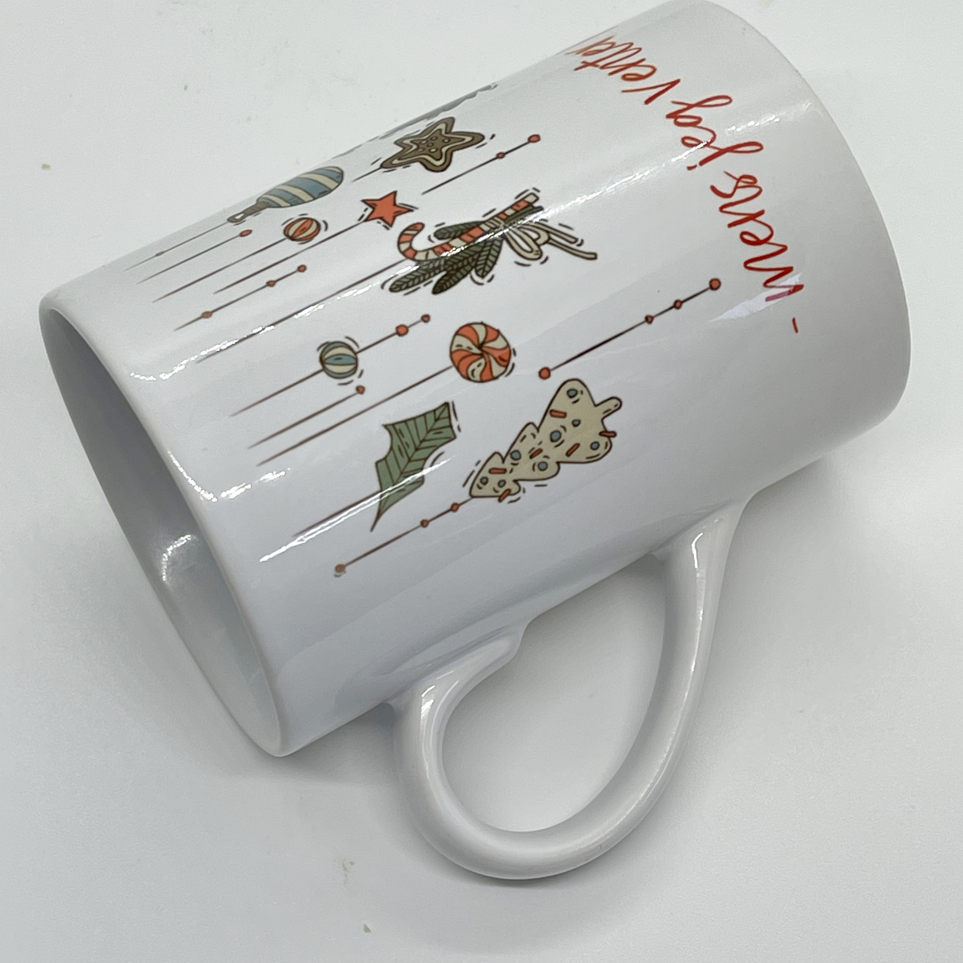 Hvitt krus i keramikk med grafisk julemotiv og håndskrevet rød tekst "-mens jeg venter på at julen skal komme". Volum: 29 cl. Diameter: 7 cm. Høyde: 10,5 cm.