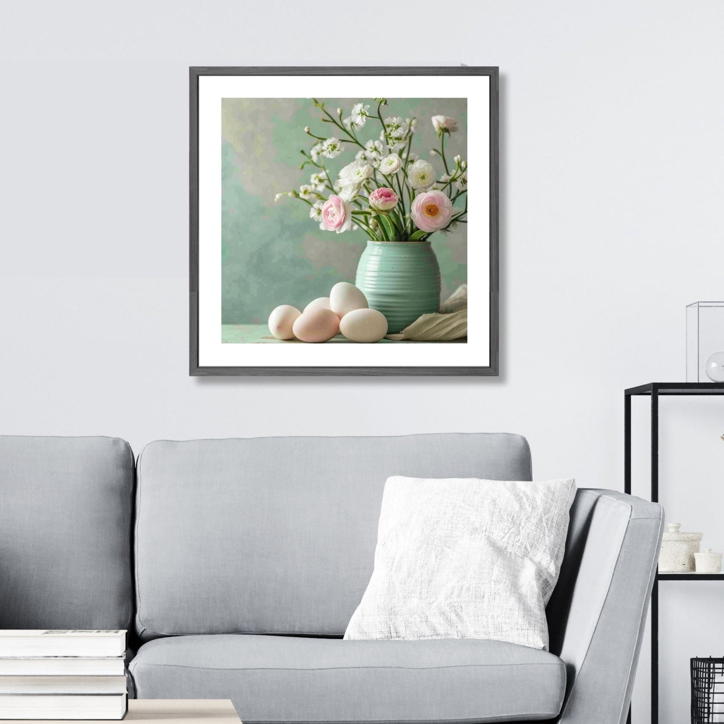 turkis vase fylt med delikate hvite og rosa blomster, perfekt supplert av flere hvite og rosa påskeegg som ligger ved siden av. Illustrasjonsfoto som viser plakat i kvadratisk format i ramme over en sofa.