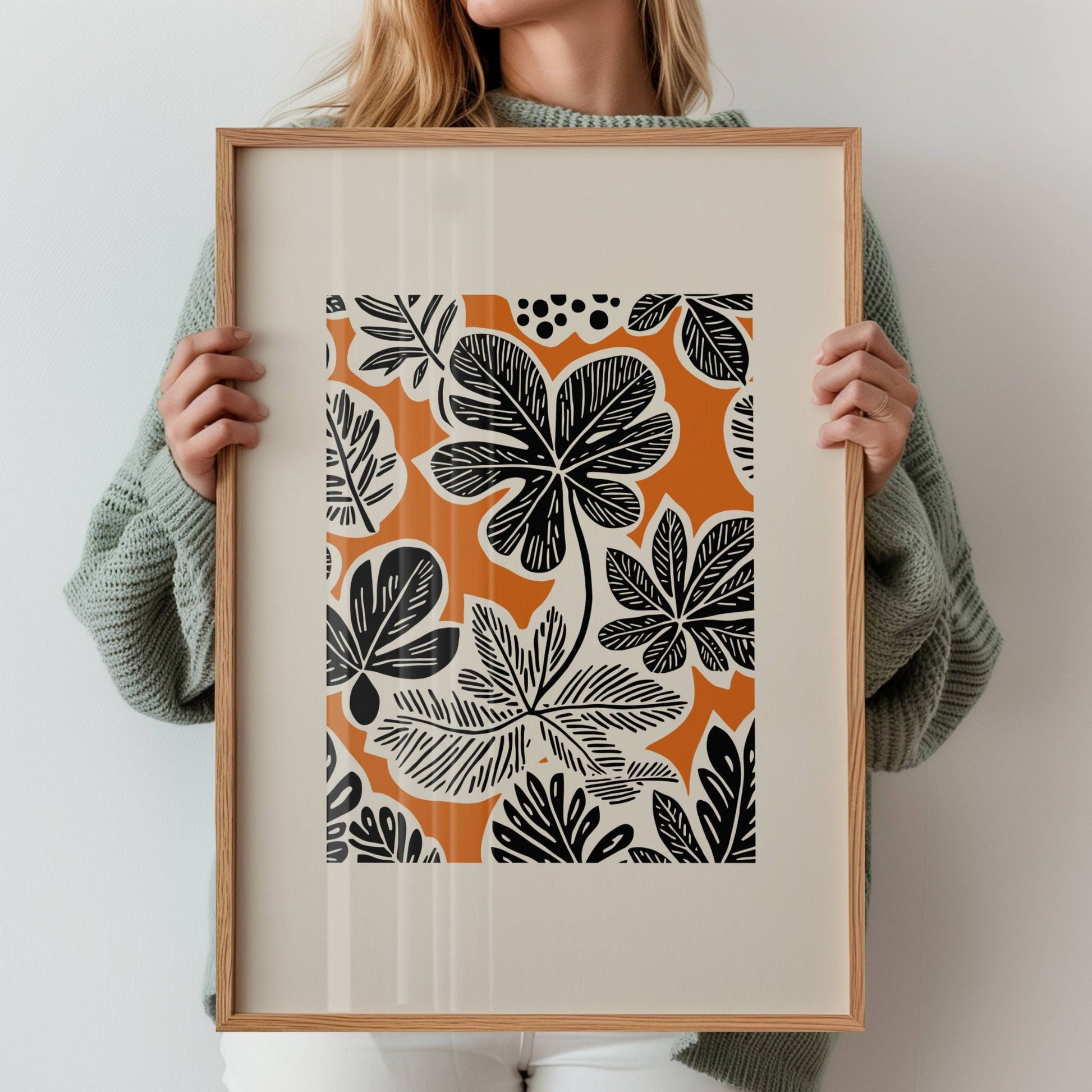 Bold Botanica kombinerer kraftige, svarte bladformer med en varm oransje bakgrunn i retroinspirert design. Illustrasjon viser motiv med bred kant i eik ramme.