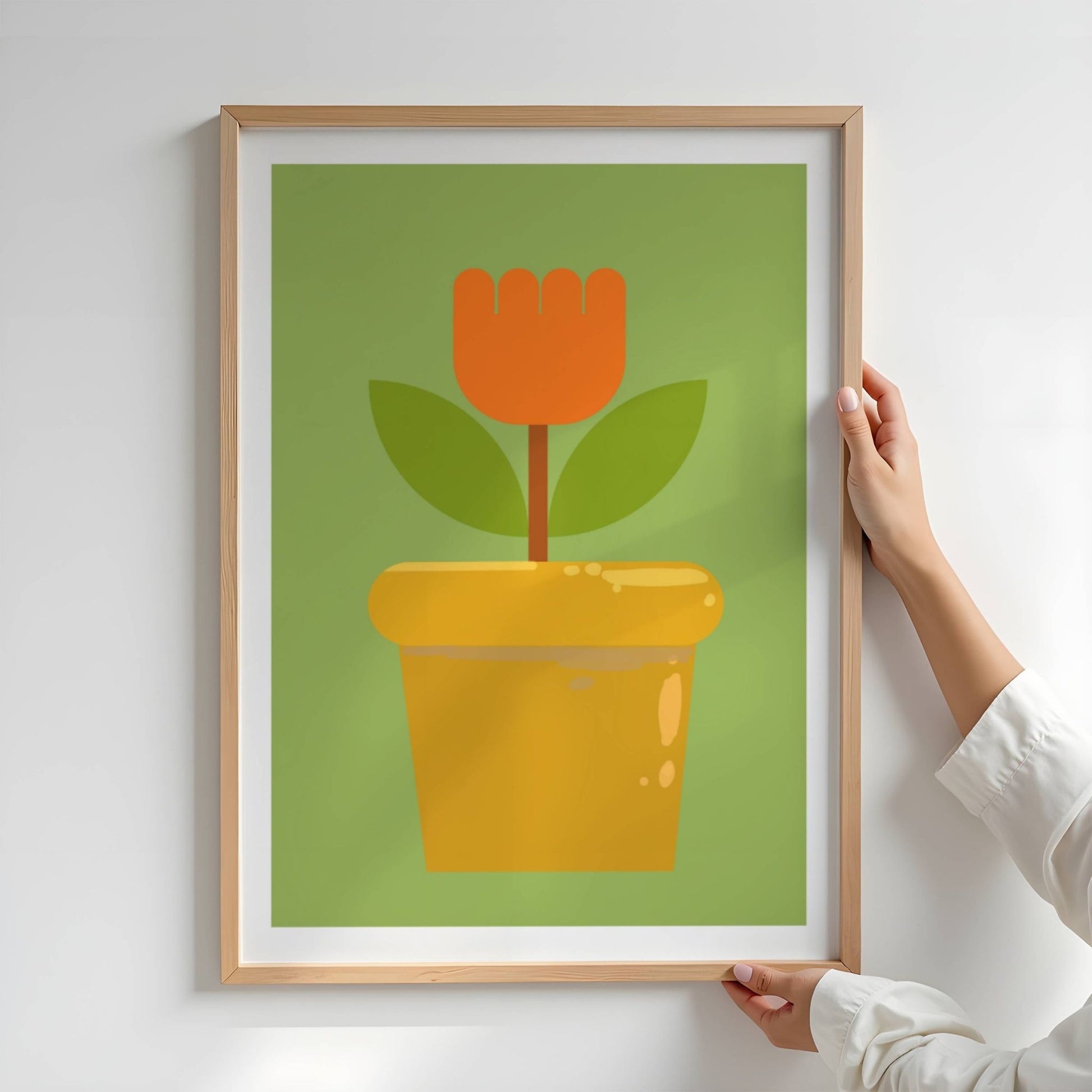 Bold Botanical No10 er en enkel og ikonisk blomst i kraftig oransje står rank i en gyllen blomsterpotte. Med to mørkegrønne blader og en stilisert form mot en frisk grønn bakgrunn, formidler motivet både retroglede og moderne minimalisme. Illustrasjon viser plakat i eik ramme.
