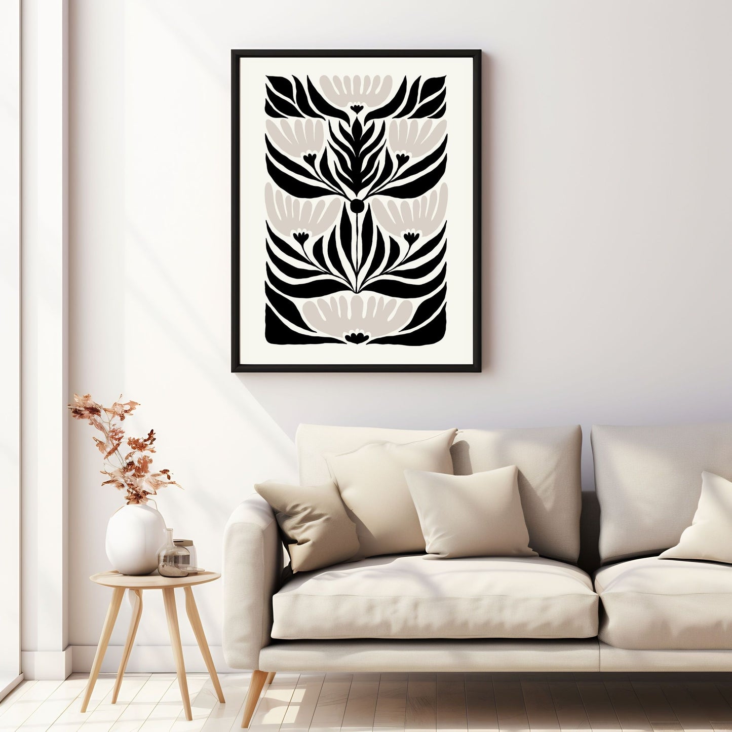 Illustrasjon av en grafisk plakat i abstrakt, floralt mønster i sort, beige og dempet hvit bakgrunn. Plakaten har en bred kant i samme som bakgrunnsfarge, og henger i sort ramme på en vegg over en sofa.
