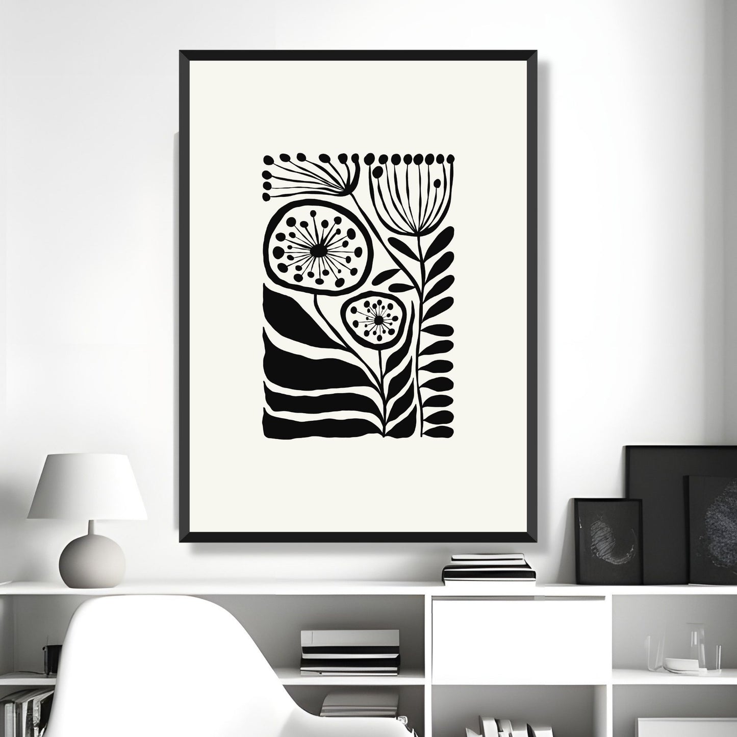 Bildet viser en grafisk plakat i abstrakt, floralt mønster i sort og dempet hvit bakgrunn. Plakaten har en bredt kant i dempet hvit farge rundt og henger i sort ramme på en lys vegg.